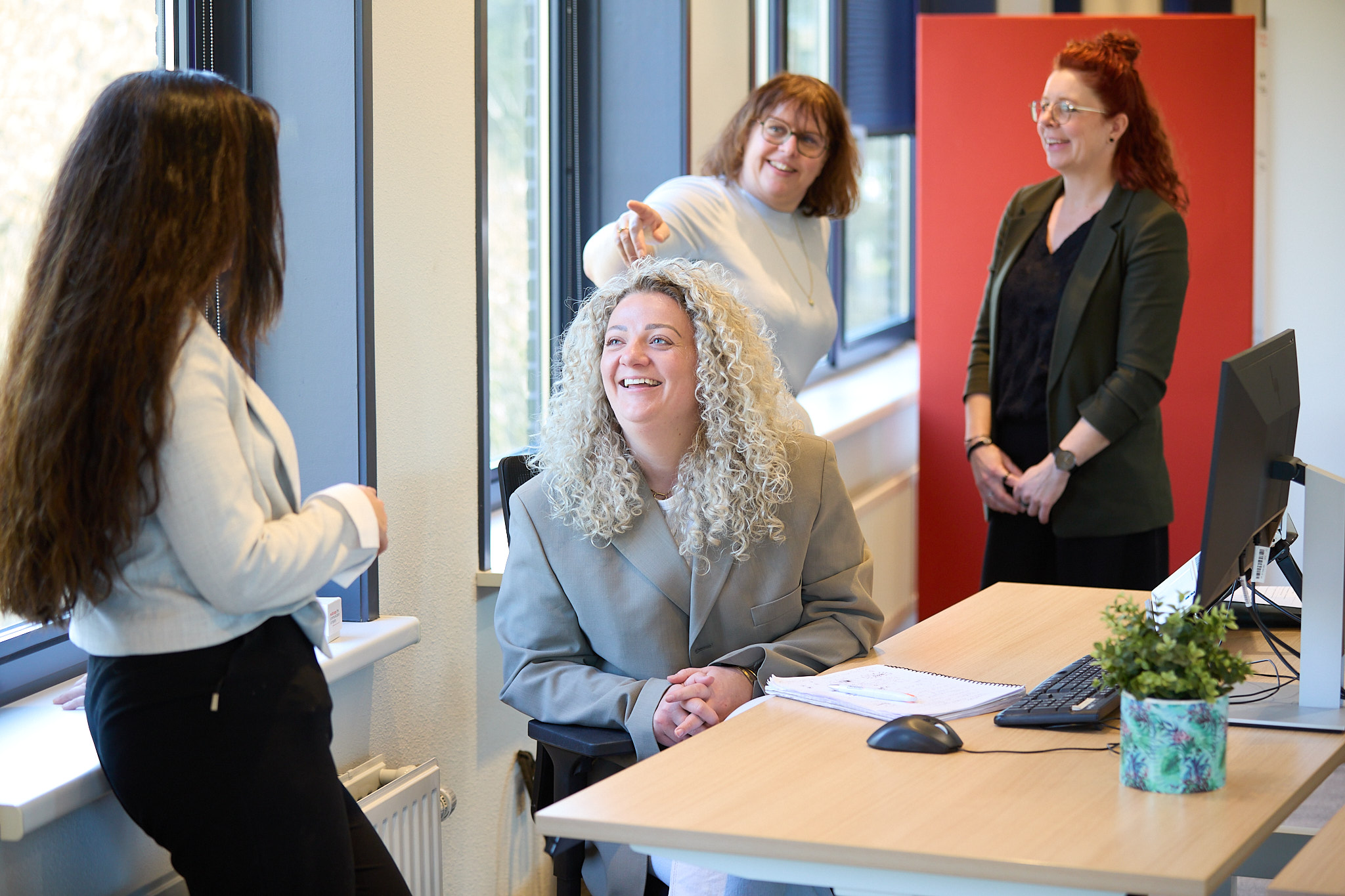 Vier vrouwelijke teamleden bespreken dossier bij werkplek.