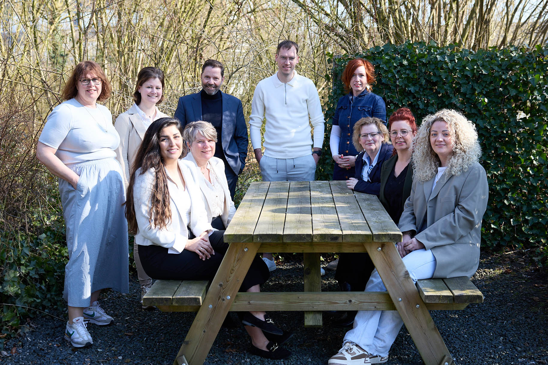Complete team van Staatvandienst AD buiten rond een picknicktafel, ontspannen en in gesprek.